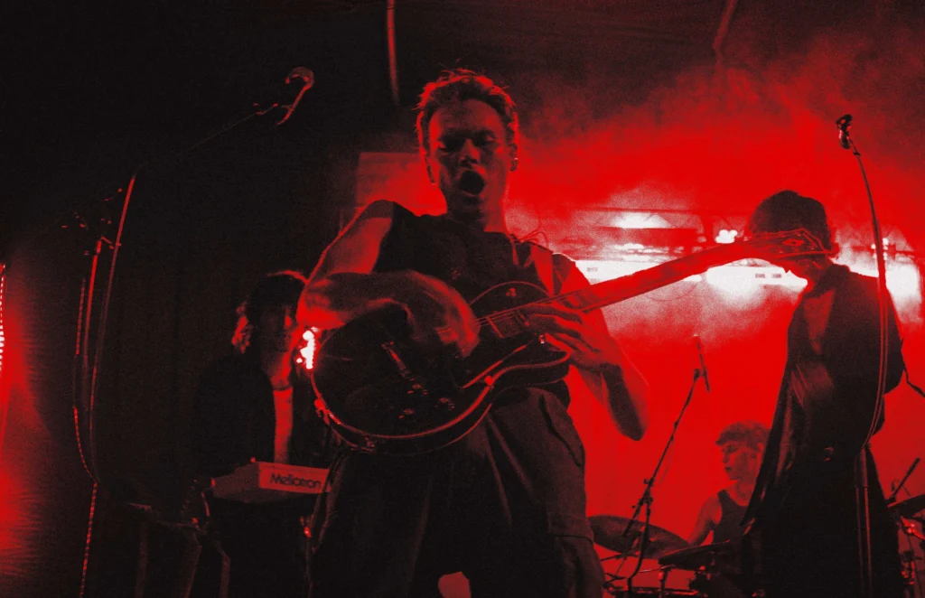 Thierry Bill mit Gitarre auf der Bühne, in rotes Licht getaucht