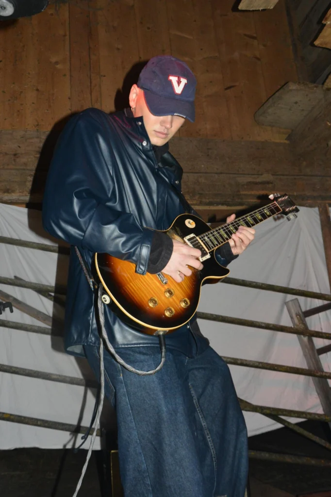 Thierry Bill in Lederjacke und Cap spielt E-Gitarre in einer Scheune