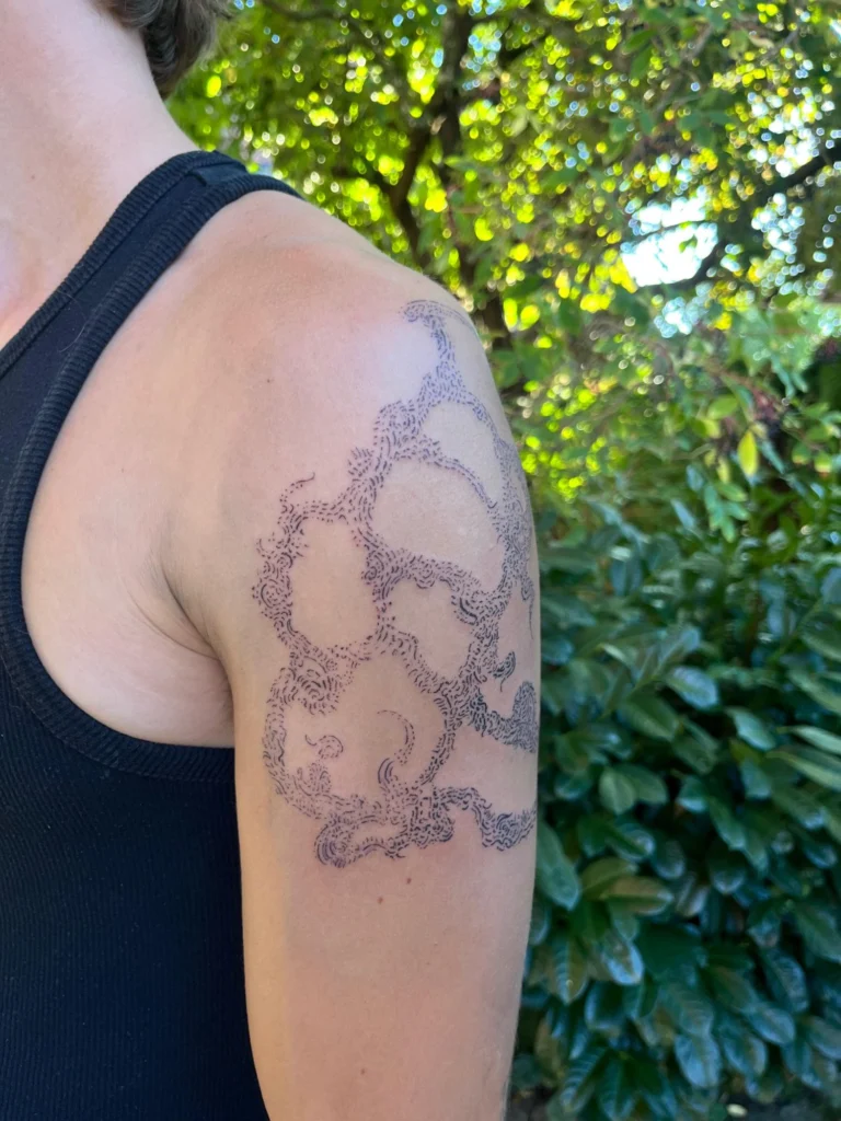 Linework-Tattoo von Thierry Bill an der Schulter: wolkenartige Formen aus feinen Strichen und Punkten