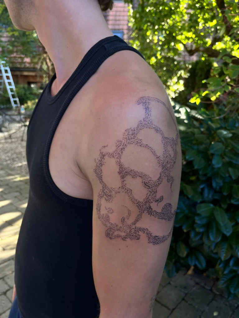 Schulter-Tattoo von Thierry Bill aus feinen Strichen, seitlich fotografiert im Garten